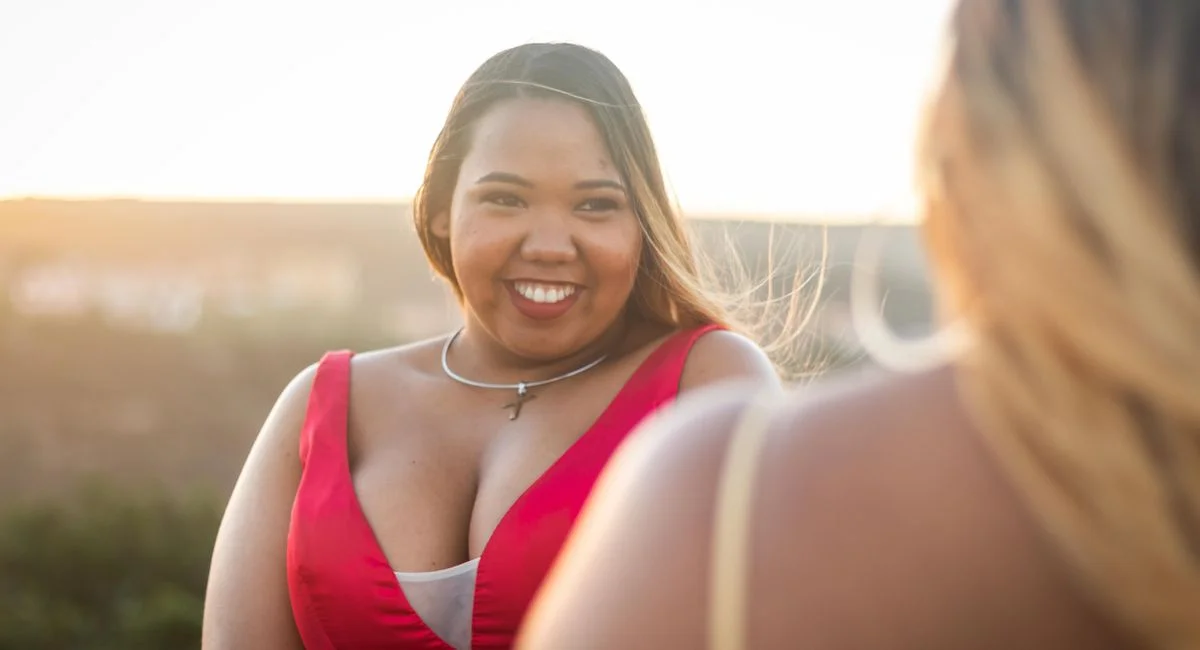 Young content chubby African American female with big breasts in elegant wear looking at crop anonymous friend under sky