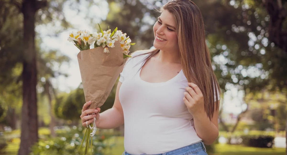 A cheerful woman holding a bouquet of flowers enjoys a sunny day in the park.