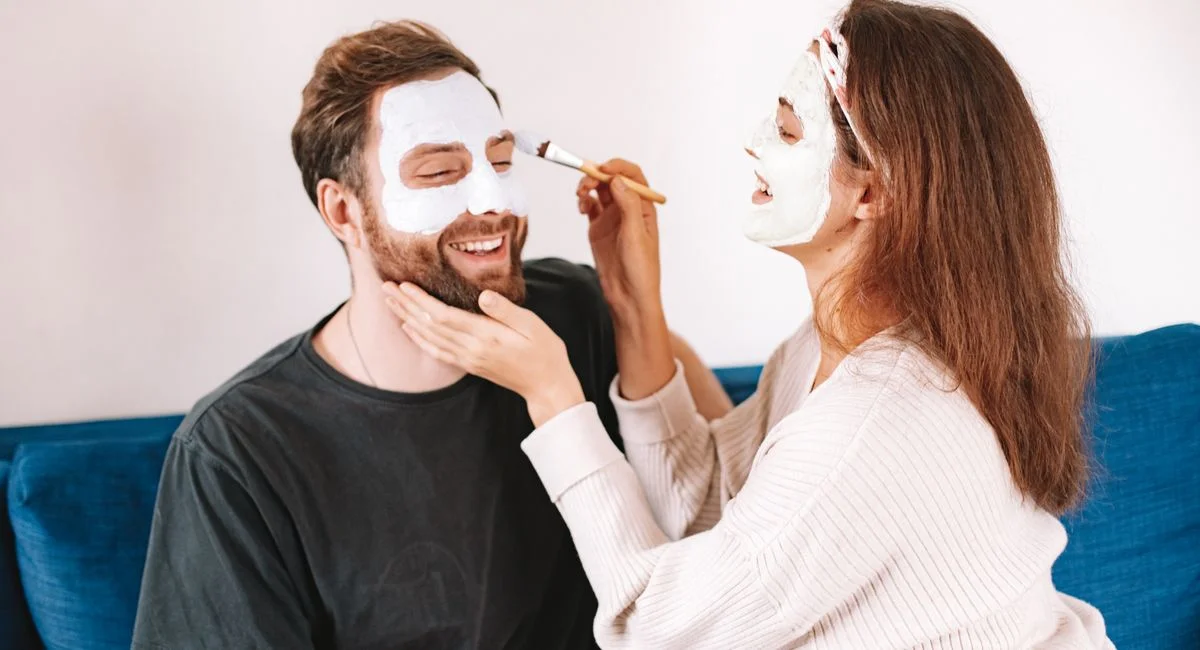 A happy couple applying facial masks together, highlighting joy and skincare in a cozy home setting.