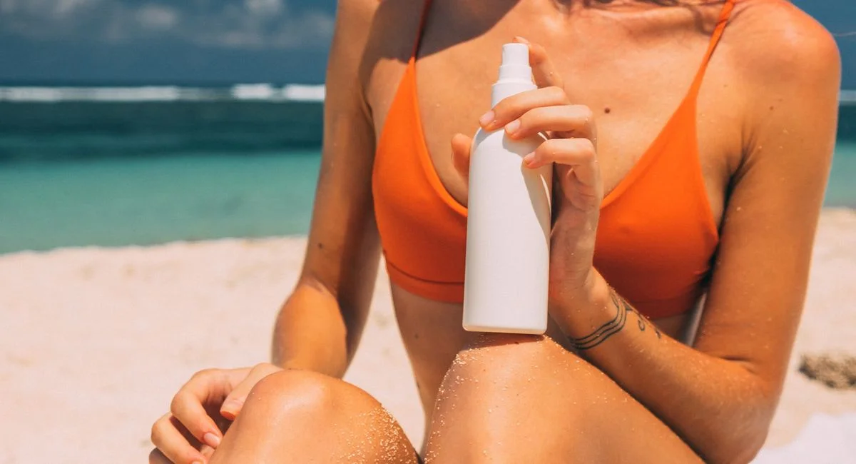 Woman applying sunscreen on a sunny beach, emphasizing skin protection and summer vibes.