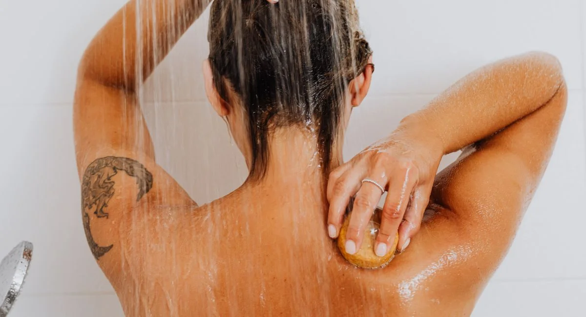 Woman scrubbing back under flowing shower water, showcasing body care routine.