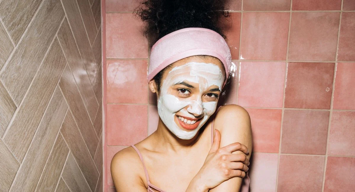 Cheerful young woman enjoying self-care routine with a face mask.