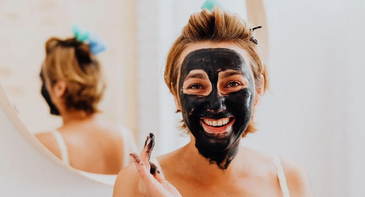 A woman enjoying skincare routine with a black cosmetic face mask indoors.