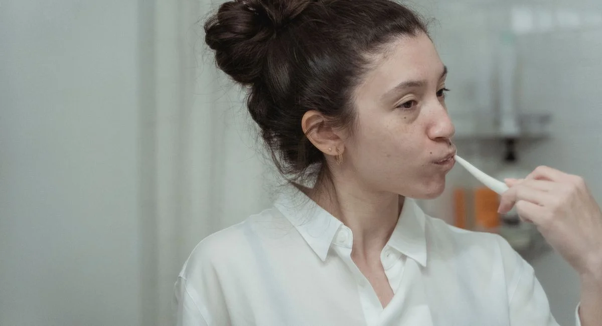 A woman brushes her teeth in the bathroom as part of her daily oral hygiene routine.