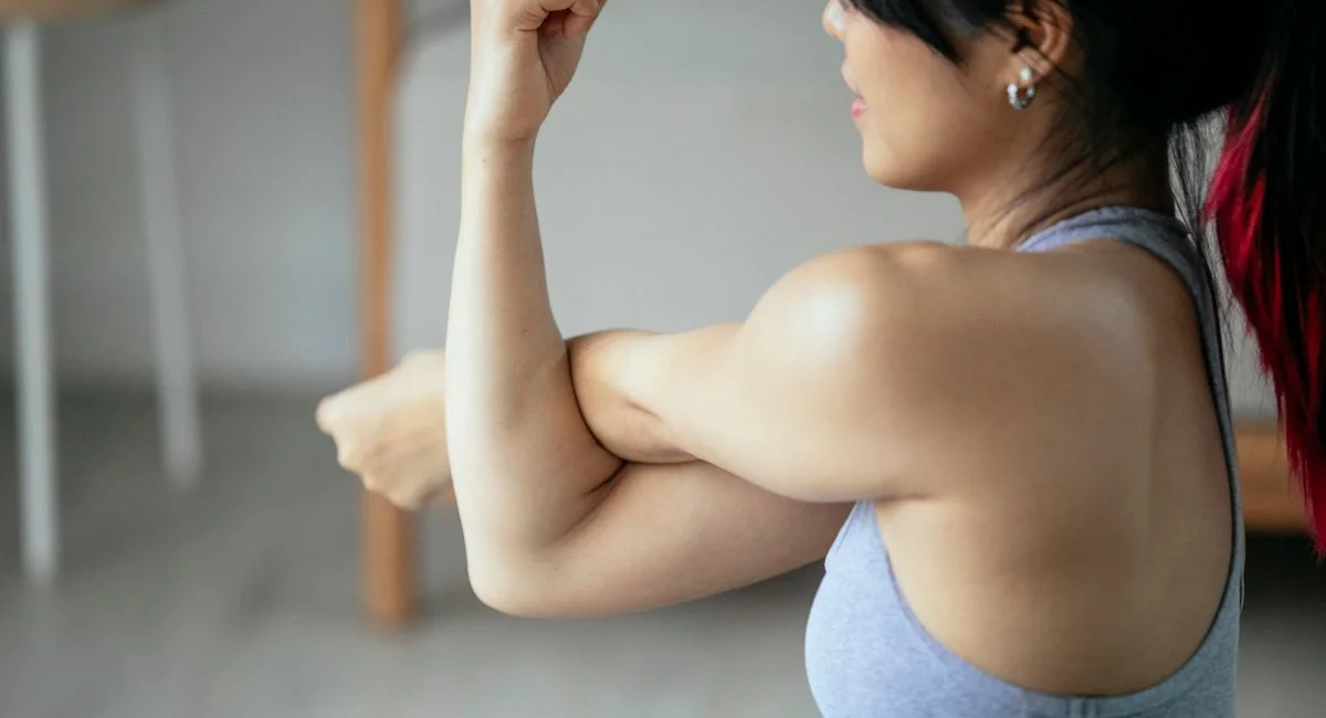 Side view of ethnic woman performing side arm stretching exercise during workout in selective focus