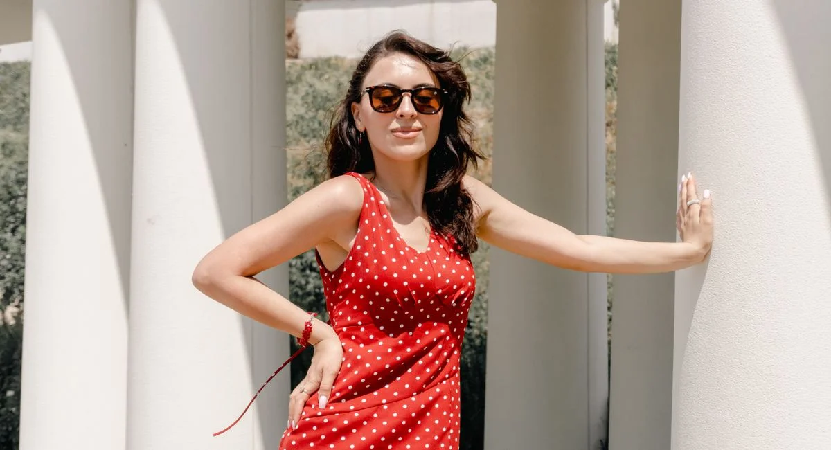 A stylish woman in sunglasses poses by white columns in sunny Baku.