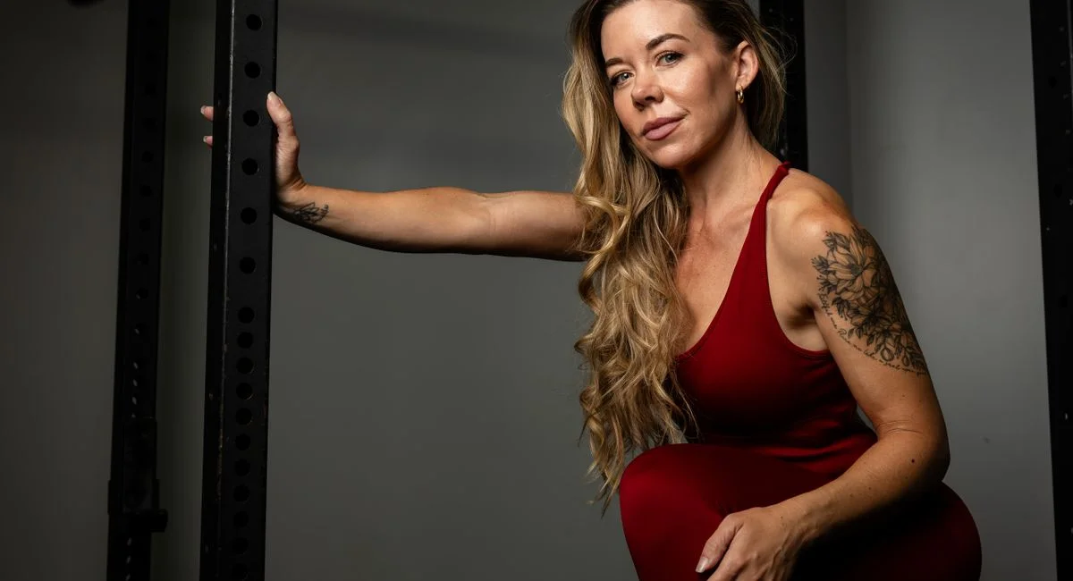 A confident woman in red activewear striking a pose indoors, showcasing strength and style.